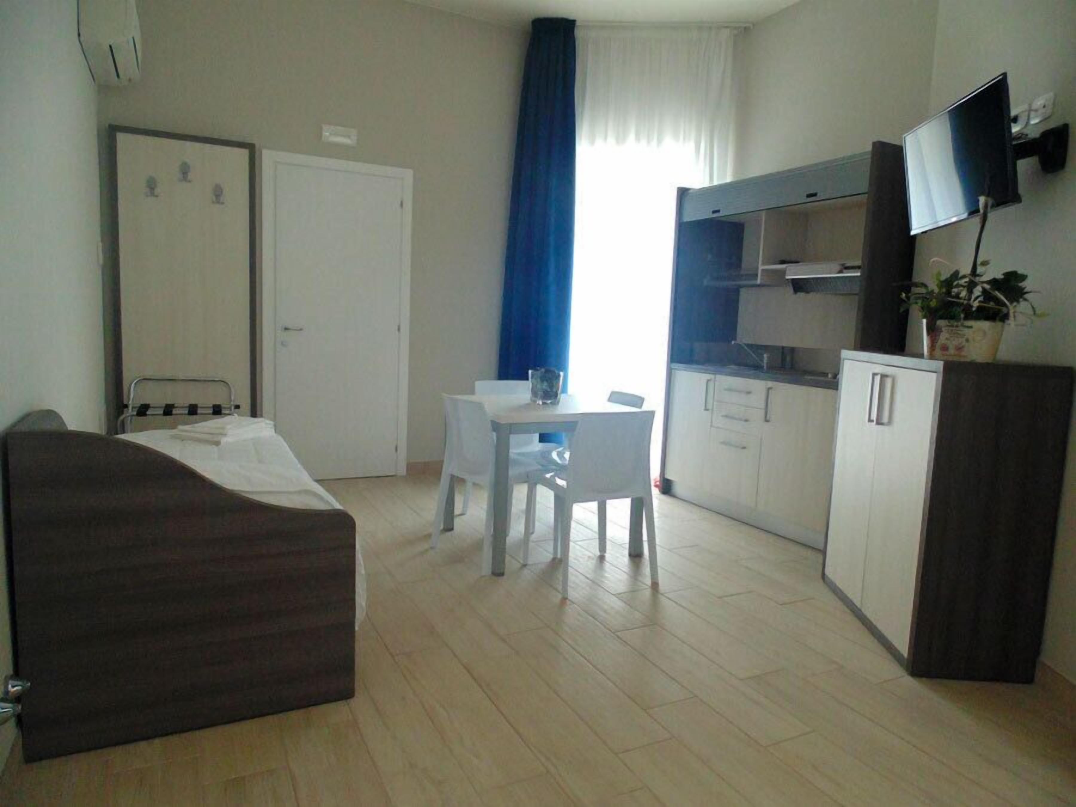 Una camera d'albergo compatta con un letto, una scrivania, una sedia, una TV e angolo cottura.
