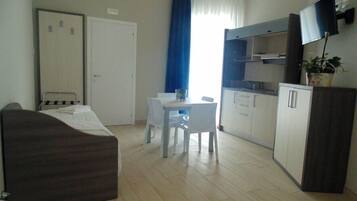 Una camera d'albergo compatta con un letto, una scrivania, una sedia, una TV e angolo cottura.
