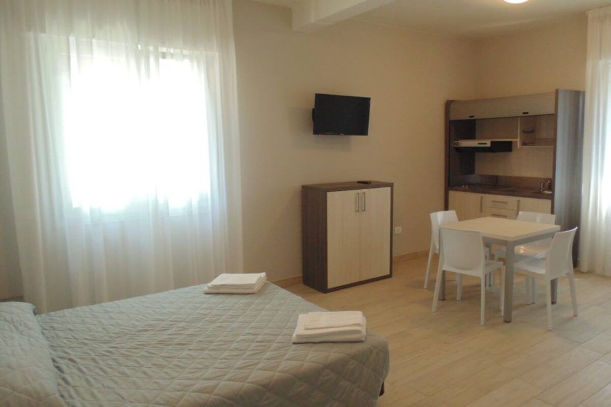 A hotel room with a bed, a desk, a chair, a television, and a kitchenette.