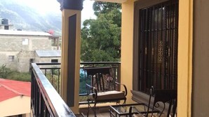 A balcony with a table and chairs, a view of the mountains, and a building in the background.