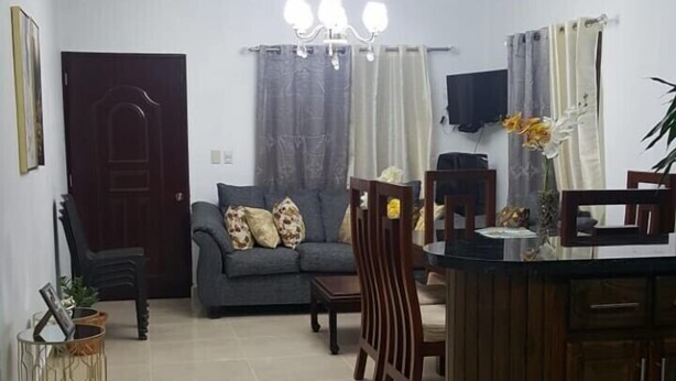 A living room with a sofa, a dining table with chairs, a TV, and a chandelier.