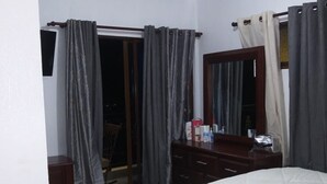 A bedroom with a bed, a dresser, a mirror, and a door leading to a balcony.