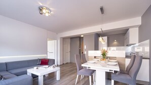Ein modernes Wohnzimmer mit grauem Sofa, einem weißen Couchtisch und einem Essbereich mit weißem Tisch und grauen Stühlen.