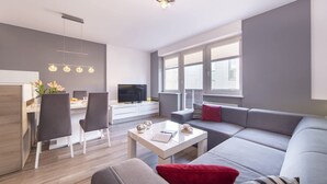 Ein modernes Wohnzimmer mit einem grauen Sofa, einem weißen Couchtisch und einem Essbereich mit Tisch und Stühlen in Weiß.