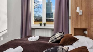 A hotel room with a large bed, a view of a historic building, and a wooden wardrobe.