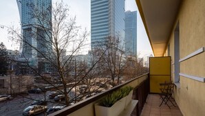 A balcony with a view of tall buildings, a tiled floor, and a potted plant.