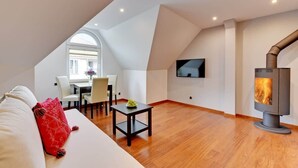 Una sala de estar moderna con un sofá blanco, una almohada roja, una mesita con un florero, un televisor montado en la pared y un estufa de leña.
