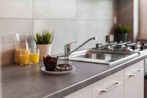 A kitchen counter with a plate of muffins, a glass of orange juice, and a potted plant.