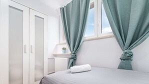A bedroom with a bed, a wardrobe, and curtains tied back to reveal a window. - Bright Apartment in the Center | Balcony and 2 Bedrooms (Warszawa)