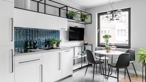 A modern kitchen with white cabinets, a black countertop, and a dining area with a round table and chairs. - Green and blue apartments (Gdansk)