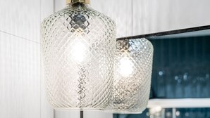 A modern pendant light fixture with a textured glass design and a brass-colored base, hanging from a black cord. - Green and blue apartments (Gdansk)