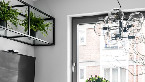 A modern dining area with a white table, black chairs, a glass chandelier, and a large window with a view of buildings. - Green and blue apartments (Gdansk)