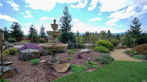 A garden with a tiered stone fountain, surrounded by various plants and trees.