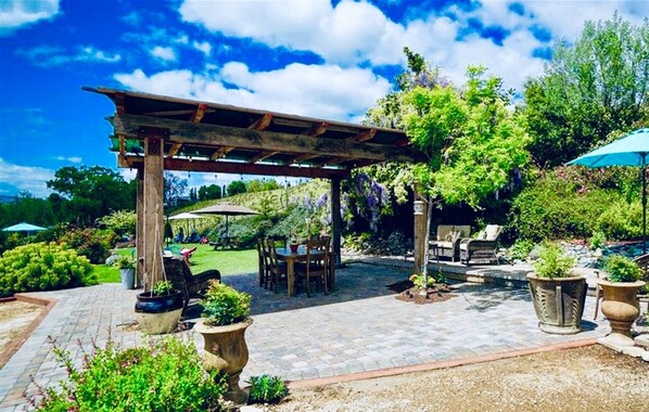A covered patio area with outdoor seating, surrounded by lush greenery and potted plants.