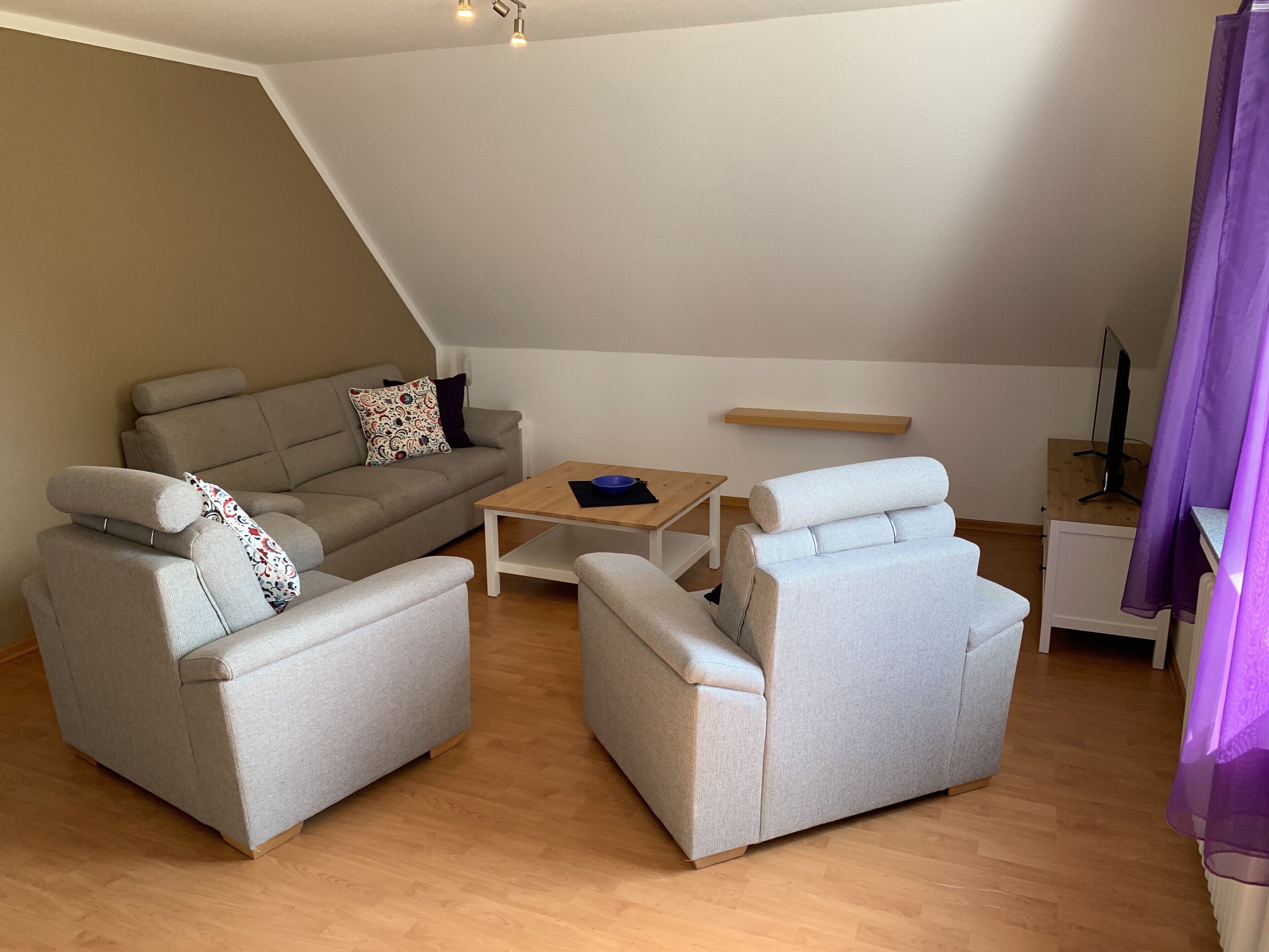 A modern living room with a sofa, two armchairs, a coffee table, and a TV stand.