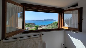 Habitación con un amplio ventanal con vistas al mar, incluyendo una playa y colinas a lo lejos.