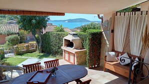Un patio con mesa y sillas, un horno de piedra y vista al mar.