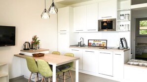 Eine moderne Küche mit weißen Schränken, einem Holzespeisetisch, grünen Stühlen und Pendelleuchten.