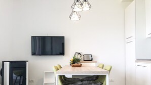 Eine moderne Küche mit Holztisch, zwei grünen Stühlen, einem an der Wand montierten Fernseher und einem Einbauofen.