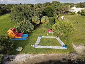 A grassy outdoor area with a large inflatable slide, a circular water play area, and a red tent.