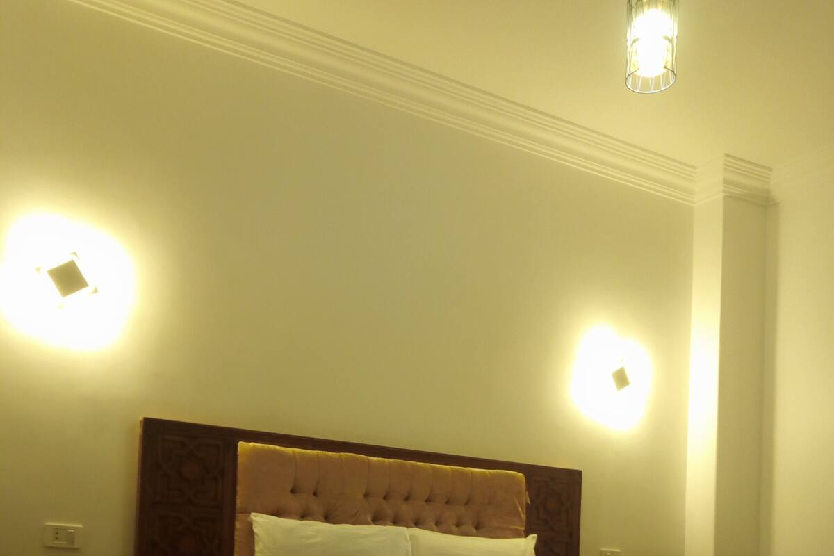 A neatly made bed with a tufted headboard, a pink and white bedspread, and two bedside lamps.
