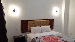 A bedroom with a tufted headboard, a bed with white bedding, a nightstand, and two wall-mounted lights. - Sydna All Hussain Hotel (Cairo)