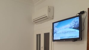A room with a mounted television displaying a landscape, a white door with a window, and an air conditioning unit on the wall. - Sydna All Hussain Hotel (Cairo)