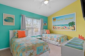 Une chambre avec deux lits, un ventilateur de plafond et une fresque murale sur le thème de la plage.