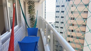 Ein Balkon mit blauen Stühlen, einer roten und grünen Hängematte und Blick auf ein Gebäude mit Balkonen.