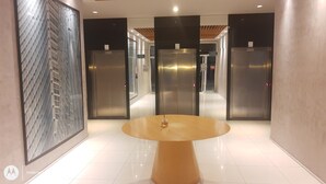 Eine moderne Lobby mit einem runden Tisch, drei Aufzügen und einem großen abstrakten Gemälde an der Wand.