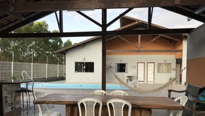 Et udendørs spiseområde med en pool, hvide plastikstole og en hængekøje.