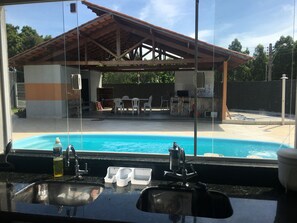Blick auf einen Pool mit einer überdachten Terrasse, Sitzgelegenheiten im Freien und einer sichtbaren Küchenzeile.