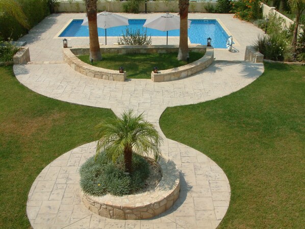 A landscaped outdoor area with a swimming pool, palm trees, and a stone pathway.