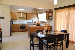 A modern kitchen with wooden cabinets, a central island, and a dining area with a glass table and chairs.