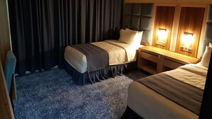 Une chambre d’hôtel avec deux lits, une tête de lit en bois, une table de chevet et une grande fenêtre avec des rideaux.
