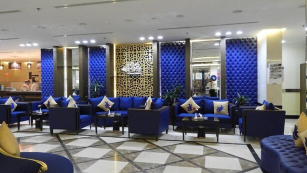 Un hall d’entrée avec des canapés et des fauteuils bleus, un mur orné de motifs et un sol carrelé.