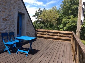 Una terraza de madera con una mesa y sillas, un muro de piedra y una valla de madera.