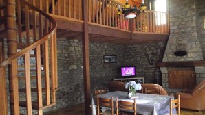 A dining area with a wooden staircase, stone walls, a fireplace, and a television. - - Ti Nominoë Cottage - (Lannilis)