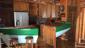 A wooden interior with a bar area, stools, a refrigerator, and a stone wall. - - Ti Nominoë Cottage - (Lannilis)