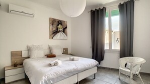A bedroom with a bed, a nightstand, a chair, a painting, and a window with curtains. - Bright 100m2 apartment in Provence with terrace (Sénas)