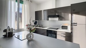 A modern kitchen with stainless steel appliances, a white countertop, and a window with curtains. - Bright 100m2 apartment in Provence with terrace (Sénas)