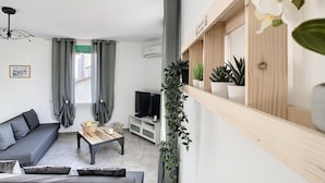 A modern living room with a sofa, coffee table, TV, and potted plants. - Bright 100m2 apartment in Provence with terrace (Sénas)