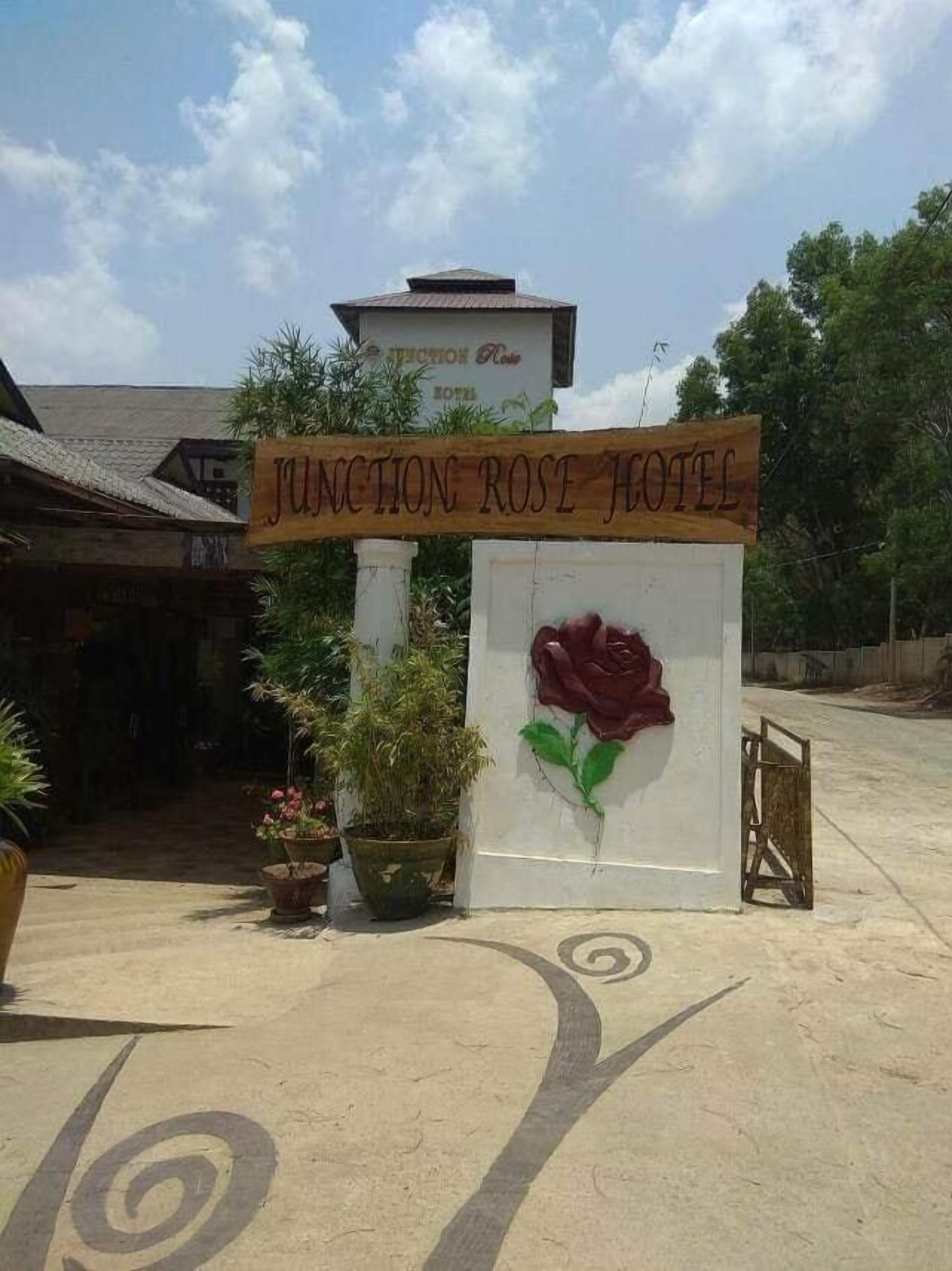 A wooden sign with "JUNCTION ROSE HOTEL" written on it, a large rose decoration, and a building in the background.