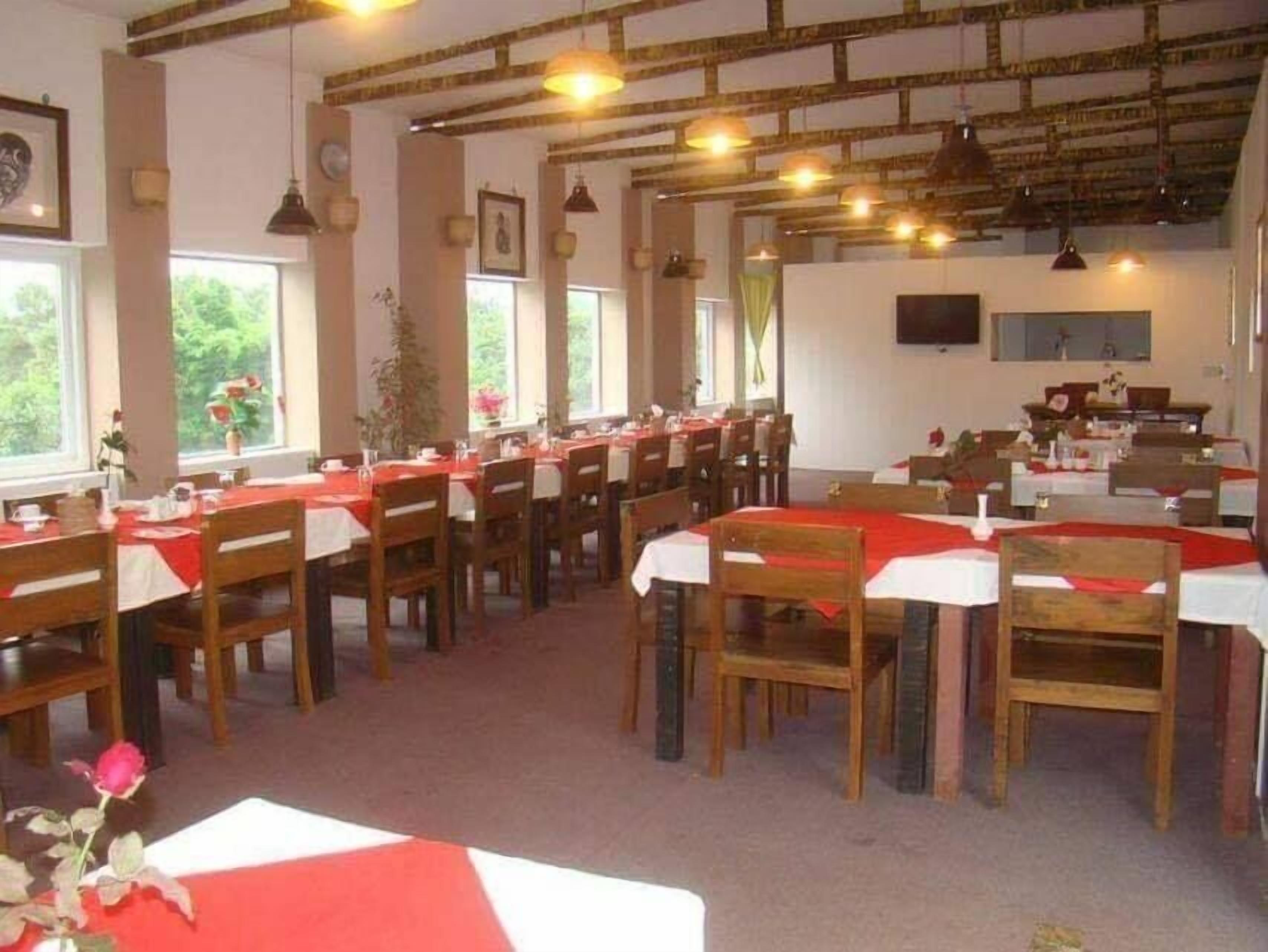Un comedor con varias mesas y sillas, ventanas amplias y lámparas colgantes.