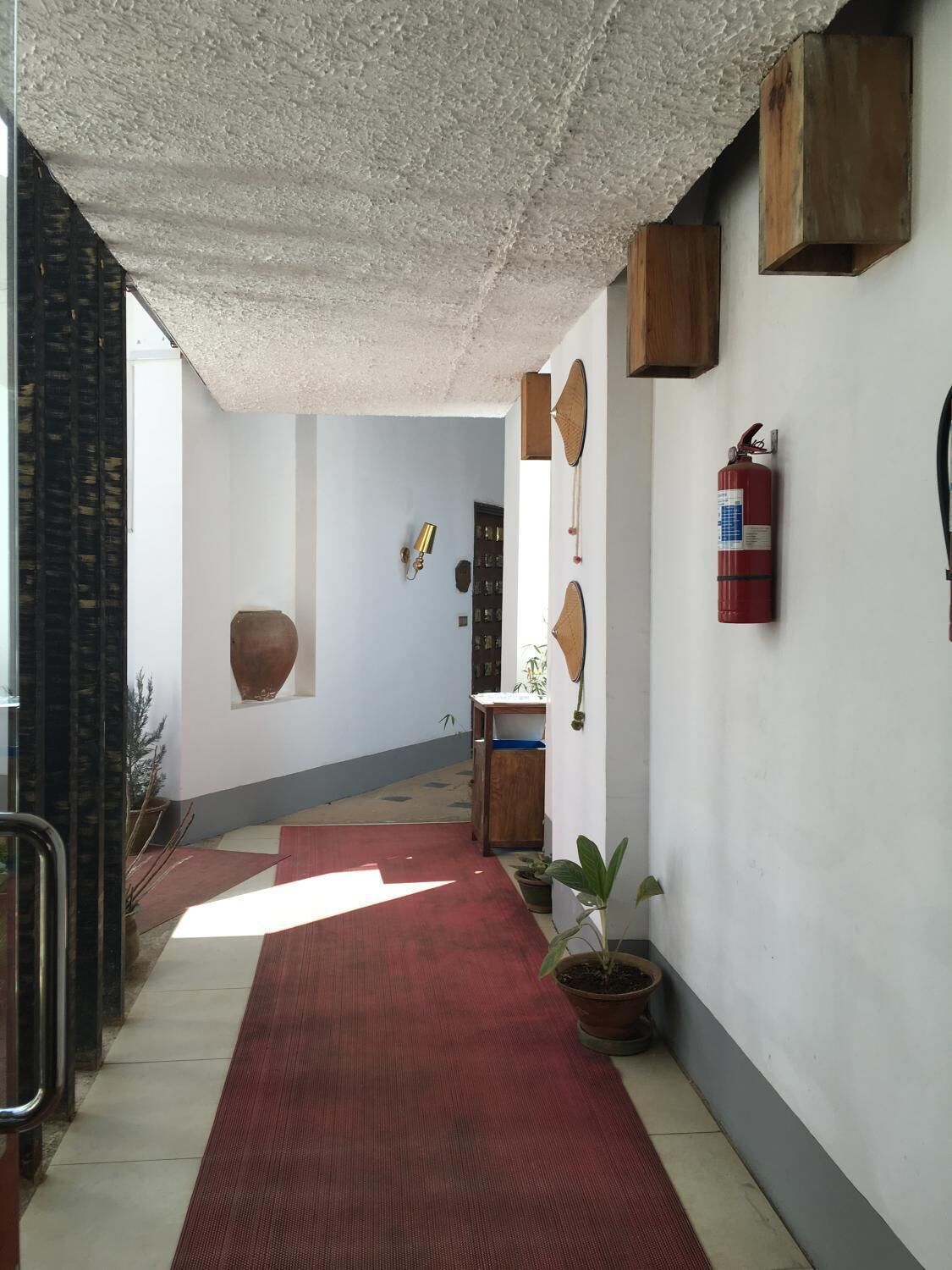 A hallway with a red carpet, a fire extinguisher, and a wooden cabinet.