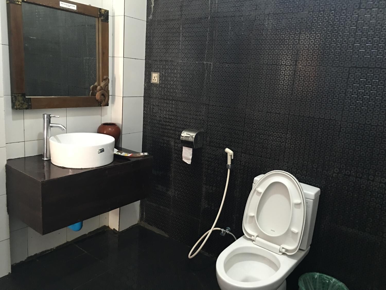 Een badkamer met een wit wastafel, een spiegel, een toilet en een wand betegeld met zwarte tegels.