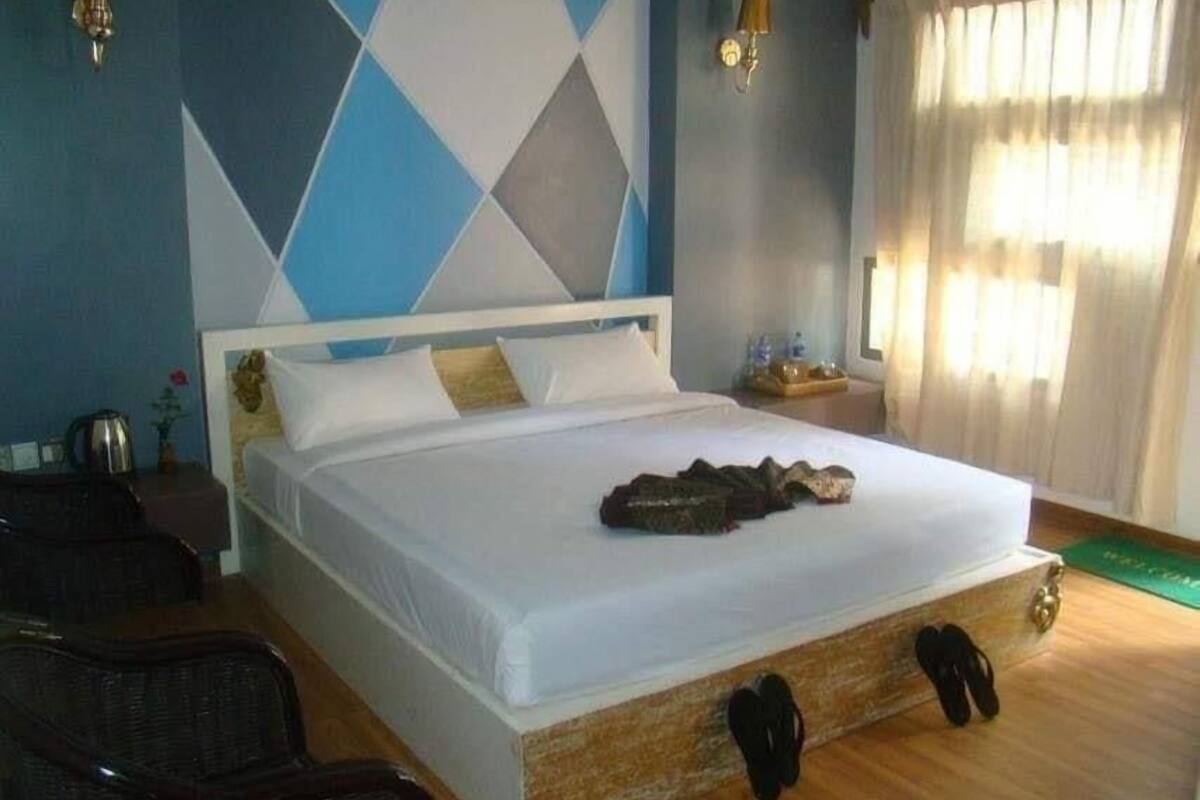 A hotel room with a large bed, a wooden floor, a wall with geometric patterns, and a window with curtains.