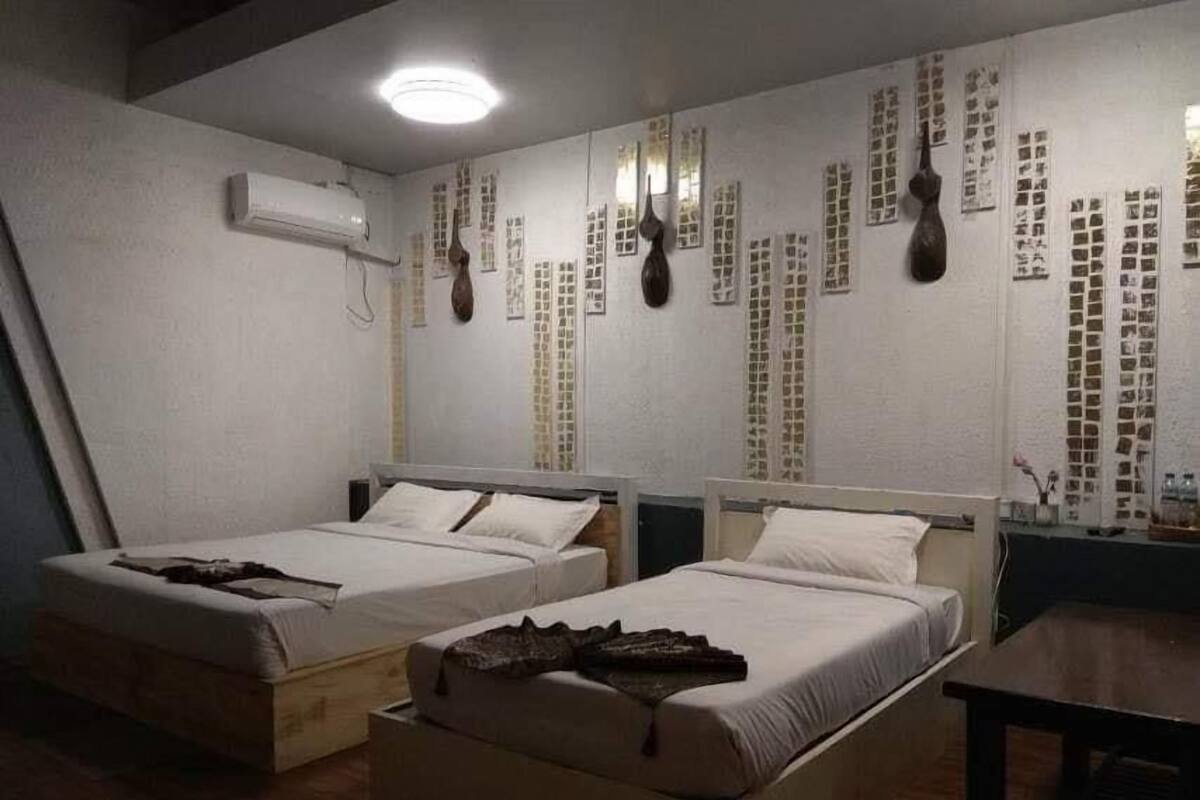 A room with two beds, a wooden floor, and a wall decorated with vertical panels.