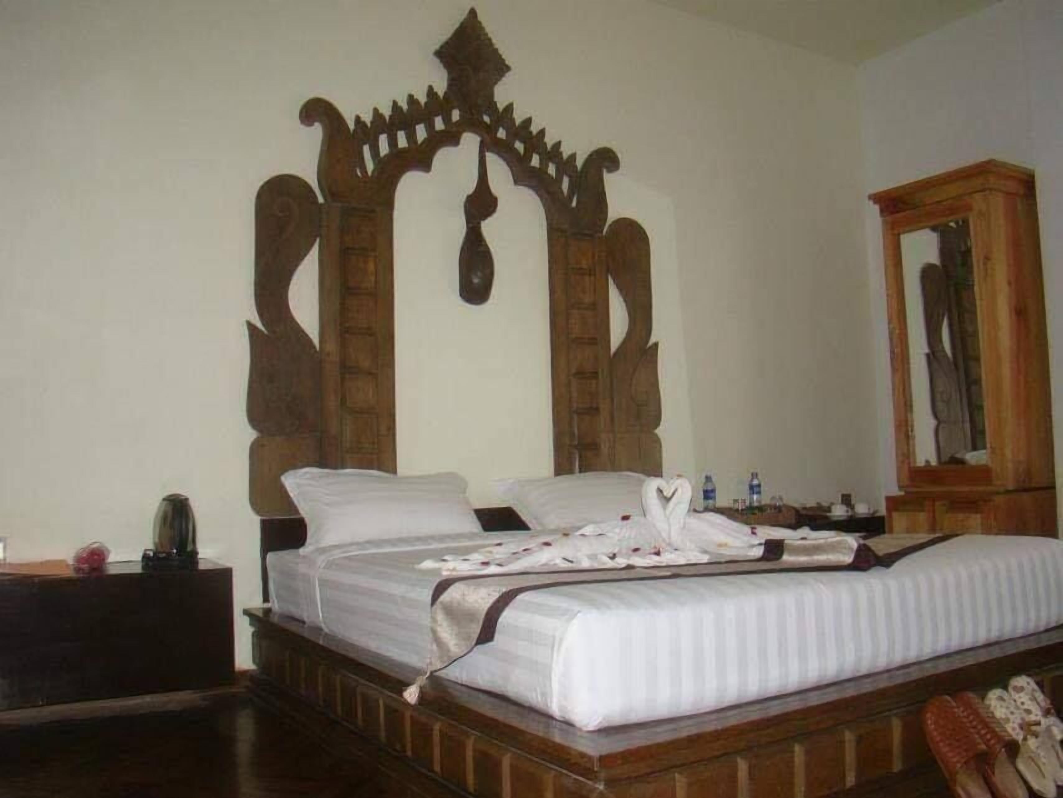 A room with a bed, a wooden headboard, a nightstand, a mirror, and a wardrobe.