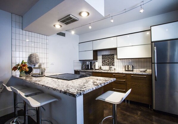 A modern kitchen with a granite countertop, stainless steel appliances, and bar stools.